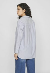 Camisa de botones a rayas hecha de una tela ligera; cuenta con un cuello, mangas largas y un corte relajado con un dobladillo curvado.