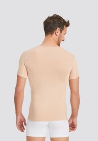 Light beige short-sleeve shirt with a snug fit, smooth texture, and round neckline. Features seam details and a minimalist design.