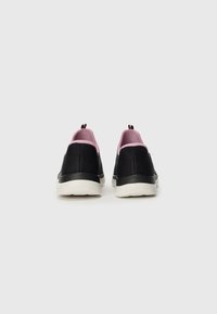Juoda pora slip-on sportbačių su rožiniu vidiniu pamušalu ir baltais kaliošais, matomi iš nugaros, prieš paprastą baltą foną.