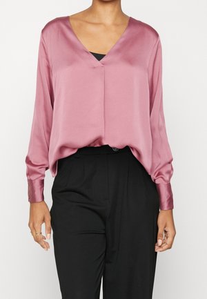 Bluzka z długim rękawem i głębokim dekoltem w kształcie litery V, wykonana z miękkiego, wrzosowego satyny, swobodnie układająca się na czarnych spodniach z wysokim stanem, z mankietami zapinanymi na guziki.