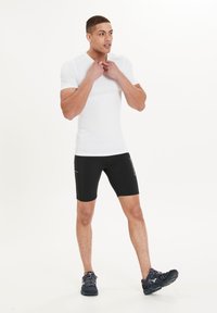 Mannen sportkleding bestaande uit een aansluitend wit T-shirt met korte mouwen en zwarte sportshorts met een zijzak, beide gemaakt van rekbare materialen.