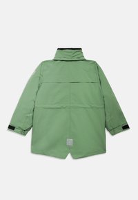 Πράσινο αδιάβροχο μπουφάν με ψηλό γιακά, πίσω άνοιγμα, στρογγυλή ετικέτα λογότυπου και ρυθμιζόμενους καρπούς. Λείο υλικό και σύγχρονος σχεδιασμός.
