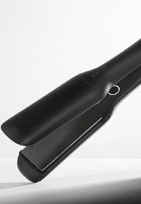 Lisseur ghd max noir avec plaques larges et bouton d'alimentation lumineux sur une surface et un fond blancs.