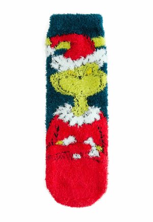 Fuzzy socks featuring a cartoonish green character in a red Santa hat, set against a dark blue background with white and red accents.