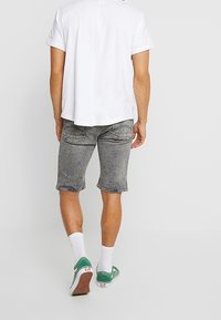 Shorts de mezclilla gris con un corte relajado, combinados con una camiseta blanca de cuello redondo. El atuendo incluye calcetines blancos y zapatillas verdes.