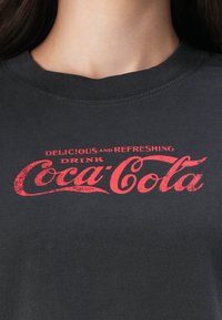 Black cotton t-shirt featuring the red text "Delicious and Refreshing Drink Coca-Cola" in distressed vintage style. Short sleeves, crew neck.