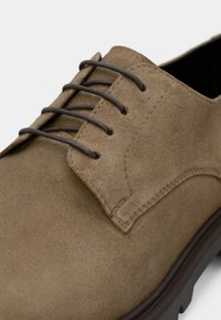 Καφέ δερμάτινο παπούτσι οξφόρντ με σκούρα καφέ κορδόνια, με στρογγυλεμένη μύτη και διακριτικές ραφές στο πάνω μέρος και στη σόλα.