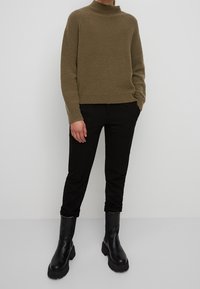 Bruine, gestructureerde trui met een hoge hals, gecombineerd met zwarte, aansluitende broek en stevige zwarte laarzen. Eenvoudig ontwerp richt zich op comfort.