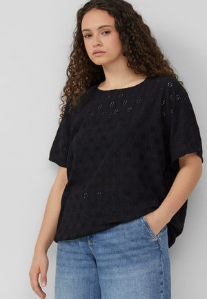 Zwarte, kortekraag top met een bloemen oogjespatroon. Ontspannen pasvorm, ronde halslijn en lichte textuur, gecombineerd met blauwe denim jeans.
