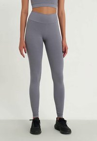 Šedé, texturované legíny s vysokým pasem a přiléhavým střihem, které jsou doplněny o odpovídající sportovní podprsenku a černé sportovní boty.