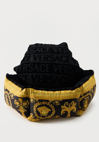 Μαύρο και χρυσό κρεβάτι κατοικίδιου Versace με μοτίβο κεφαλής Μέδουσας και κείμενο "VERSACE" στο ανυψωμένο επενδυμένο προσκέφαλο.
