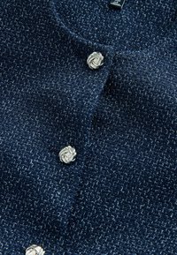 Granatowy sweter kardigan z tkaniny o fakturze, zdobiony srebrnymi guzikami w kształcie węzłów z przodu.