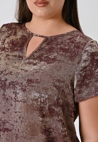 Top bordeaux con una superficie lucida e texture. Presenta un colletto keyhole e maniche corte, progettato con un motivo sottile.