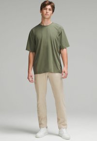Tricou scurt cu mânecă, de culoare verde măsliniu, dintr-un material moale, asortat cu pantaloni bej și adidași albi. Croială simplă, lejeră, cu guler rotund.