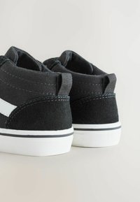 Svarta högskor i canvas med en vit rand, texturerade mockadetaljer, vita gummisulor och kontrasterande sömmar.