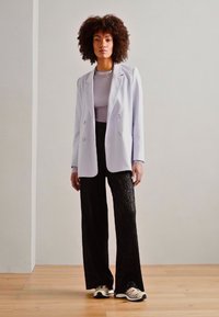 Lilla dobbelspent blazer over en lys grå topp, kombinert med svarte teksturerte vide bukser og kremfargede joggesko. Enkelt, rent design.