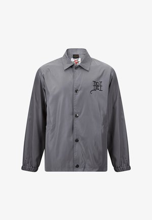 Giacca a vento grigia con colletto, chiusura frontale con bottoni, polsini elasticizzati e un logo nero stampato sul lato sinistro.