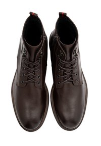 Brązowe skórzane botki za kostkę o gładkiej teksturze, okrągłym nosku, sznurowanym przodzie i dekoracyjnym okuciu po bokach.