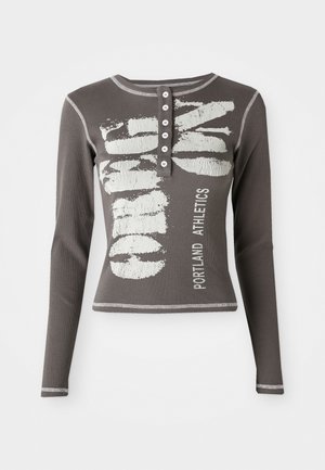 T-shirt à manches longues, ajusté, en coton gris foncé avec une texture côtelée. Il est doté d'une patte de boutonnage et d'un texte graphique blanc : "Portland Athletics."
