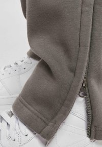 Grå bomullssweatpants har detaljer med glidelås på siden, kombinert med hvite sneakers. Stoffet er mykt med en jevn tekstur.