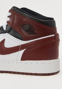 Visoke tenisice od bijele kože, s burgundskim akcentima i crnim ovratnikom. Uključuje uvršteni Air Jordan logotip na bočnoj strani.