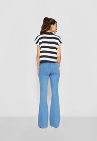 Zwart-wit gestreepte, korte mouwen cropped top in combinatie met hoogtaille, uitlopende blauwe jeans, gezien vanaf de achterkant.