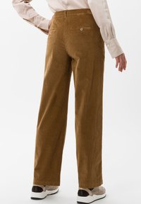 Bruna kordfläktade vida byxor med bakfickor och knappdetaljer, tillsammans med en beige topp och beige och svarta skor. Mjuk textur.