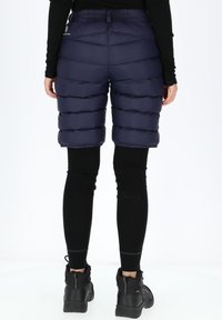 Shorts puffy blu navy con dettagli di cucitura orizzontale, lunghezza fino a metà coscia, vita elastica, abbinati a leggings neri e stivaletti neri alla caviglia.