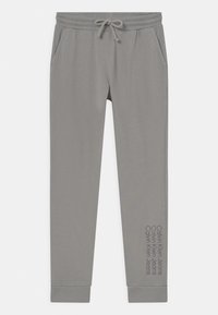 Jasnoszare dresy z elastycznym paskiem w talii i regulowanym sznureczkiem. Posiadają boczne kieszenie i nadruk "Calvin Klein Jeans" wzdłuż nogawki.