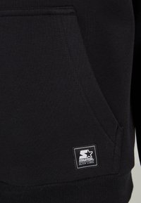Black fleece hoodie with a kangaroo pocket, ribbed cuffs, and hem. Features a square logo label in white and black on the front.