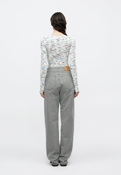 Hosszú ujjú fehér felső színes szövegmintákkal, magas derekú szürke bő szárú farmerral, barna bőrtalpra emlékeztető folttal.