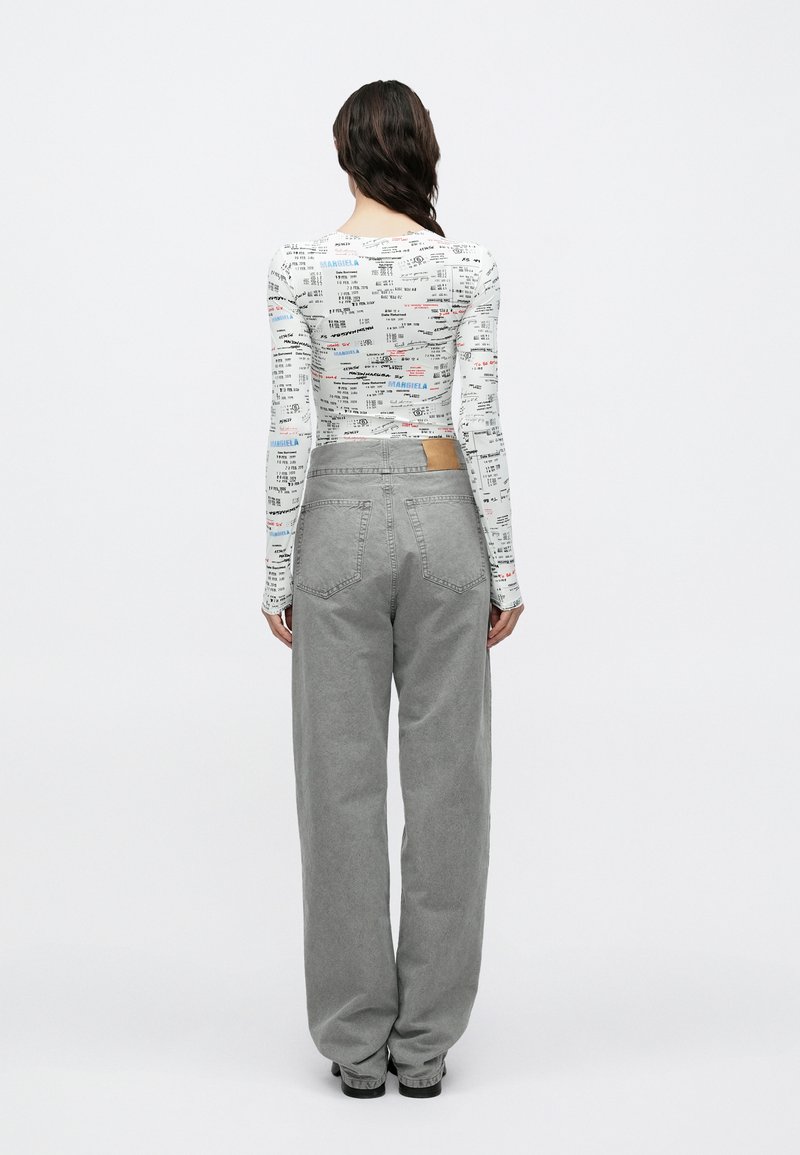 Langärmliges Oberteil in Weiß mit bunten Schriftmustern, kombiniert mit hoch taillierten grauen Jeans mit weitem Bein und einem braunen Lederetikett.