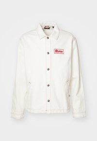 Jachetă din denim albă cu un logo roșu brodat, butoane argintii și cusături roșii în contrast, dotată cu două buzunare laterale și un guler clasic.