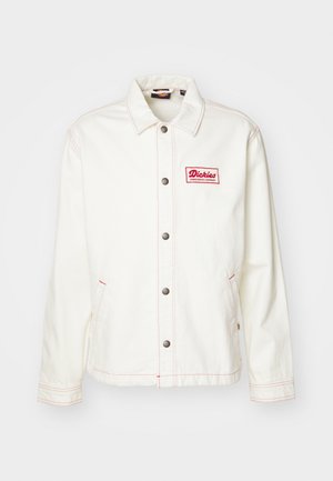 Chaqueta de mezclilla blanca con un logo bordado en rojo, botones plateados y costuras rojas en contraste, con dos bolsillos laterales y un cuello clásico.