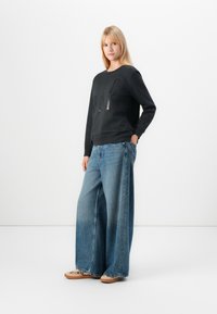 Black sweatshirt with a centered graphic, paired with wide-leg blue jeans. The fabric appears soft, with a casual fit and clean lines.