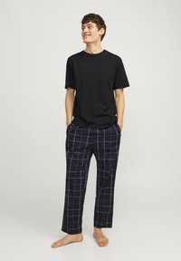 Zwart katoen T-shirt gecombineerd met marineblauwe geruite broek met witte en blauwe lijnen. Losse pasvorm; model staat blote voeten met de handen in de zakken.