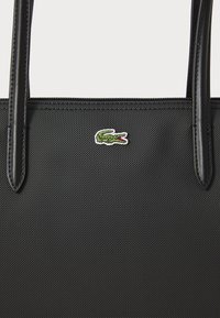 Sac fourre-tout noir en tissu texturé avec des accents en cuir lisse, présentant un logo de crocodile brodé en vert et rouge à l'avant.
