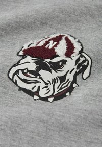 Tela gris con un bulldog bordado que lleva una gorra a rayas en color granate y blanco. Los detalles notables incluyen el collar con pinchos del bulldog y sus rasgos faciales.