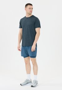 Herrarnas träningsklädsel med en mörkblå kortärmad t-shirt och lätta blå shorts. Avslutad med grå sneakers och vita strumpor.