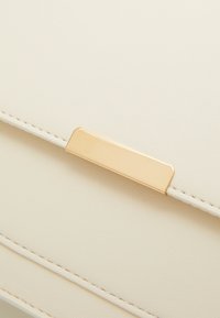 Borsa in pelle color crema con una chiusura rettangolare in metallo dorato lucido e cuciture visibili lungo i bordi.