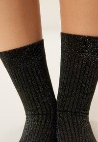 Sorte ribstrikkede sokker med metallisk glans. Blød tekstur, midt på læggen, med en struktureret øvre kant.