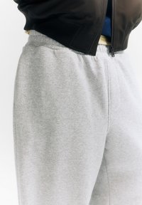 Pantaloni de trening gri din material moale, cu talie elastică și croială lejeră, cu o textură subtilă și fără modele vizibile.
