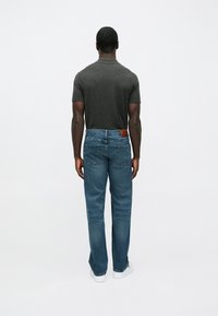 T-shirt ajustada cinza escuro, jeans de denim azuis, com corte reto padrão, um retalho de couro castanho na cintura e ténis brancos.