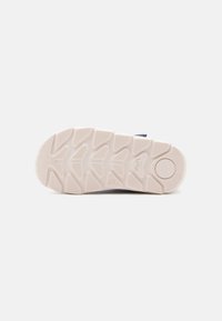 Suela de zapato con una parte inferior de goma texturizada que presenta un patrón de zigzag. Color: crema claro con un acento oscuro cerca de la zona del talón.