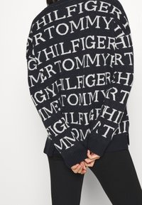 Marineblauer Strickpullover mit großem, kontrastierendem weißen "TOMMY HILFIGER"-Schriftzug. Gerippte Bündchen und Saum, lockere Passform mit seitlichen Schlitzen für mehr Komfort.