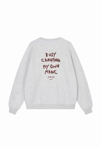 Šedá mikina s dlouhými rukávy, na zadní straně s tmavě červeným textem "ZAMĚŘENÍ NA VYTVÁŘENÍ VLASTNÍ MAGIE." Jednoduchý design, volný střih.