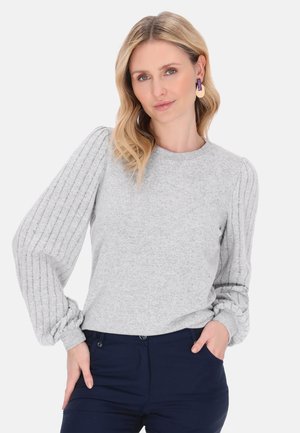 Lys grå strikket sweater med ribbede ballonærmer og rund halsudskæring, parret med marineblå bukser. Glat tekstur, afslappet design.