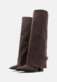 Καφέ μπότες μέχρι το γόνατο με λεία υφή, μυτερή μύτη και τακούνι τύπου block. Διαθέτουν ασημένια αγκράφα στο εξωτερικό μέρος.