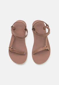 Brown flat sandals featuring a simple design with two adjustable straps. Soft footbed and minimalistic style, suitable for casual wear.