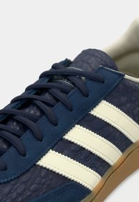 Navyblauwe sneaker met een bovenwerk van getextureerd leer, witte strepen en ronde veters. Voorzien van een rubberen zool en suède accenten nabij de tong.